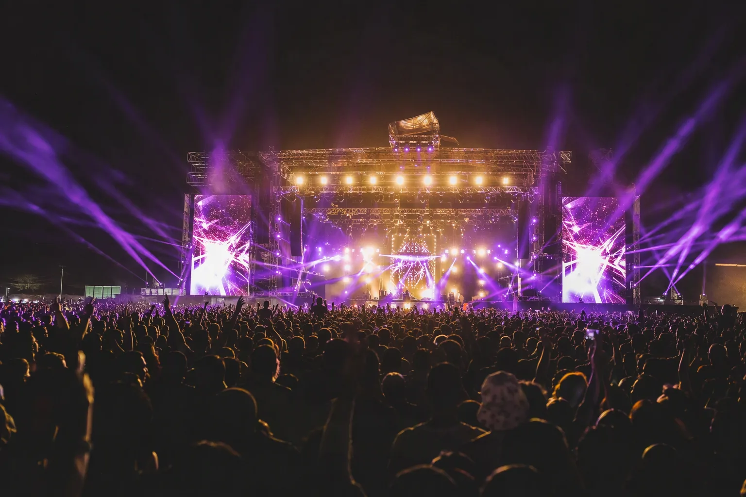 An outdoor concert stage glowing in purple and gold light over a night crowd on a Lusaka polo field