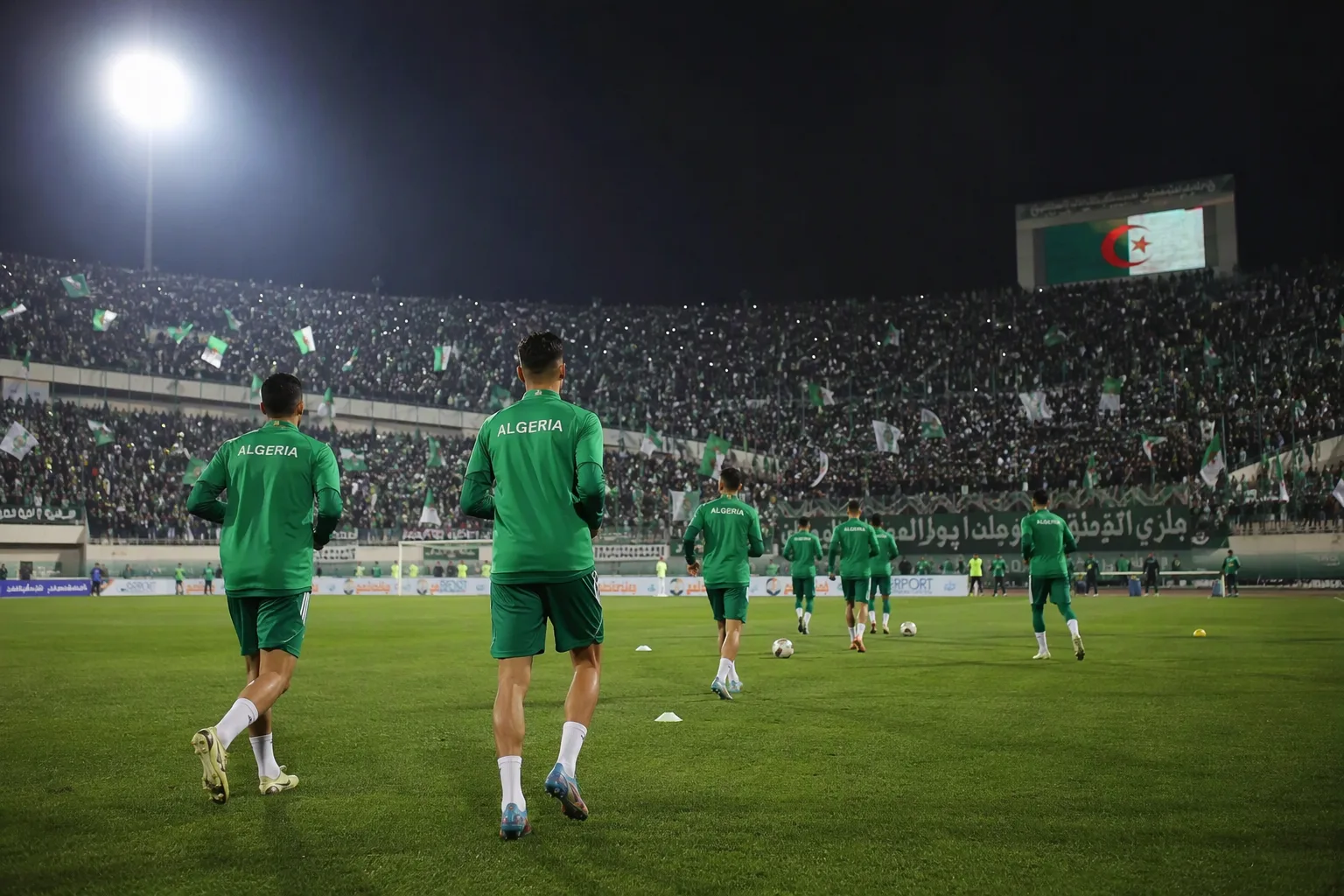 A floodlit North African stadium at night with players warming up