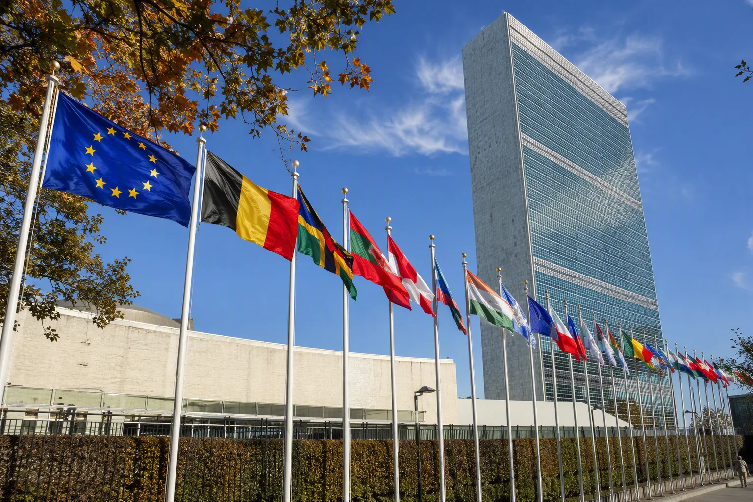 The European Union flag flying among member-state flags outside a glass headquarters building