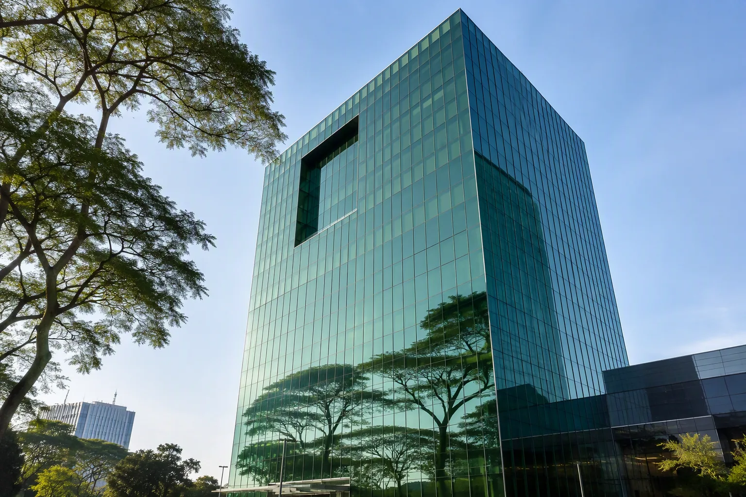A modern glass bank headquarters tower reflecting trees, symbolising green finance